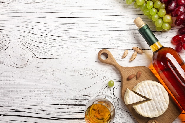 White wine bottle, grape, cheese and wineglass on white wooden board