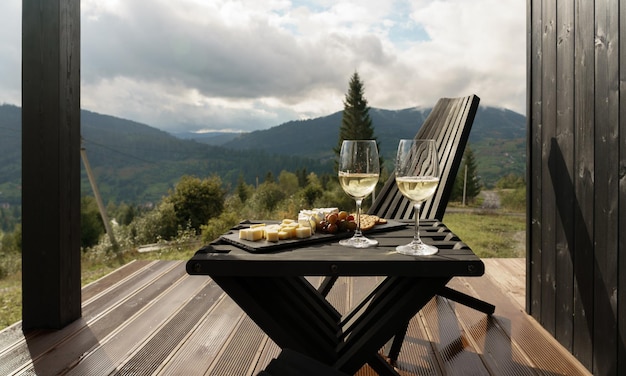 White wine glasses and plate of cheese on terrace with mountains view with copy space