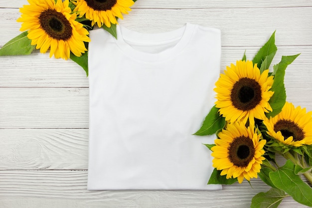 White womens cotton folded T Shirt mockup with sunflowers on white wooden background. Design t shirt template, print presentation mock up. Top view flat lay.