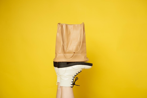 White womens shoes hold a beige bag on a yellow isolated background