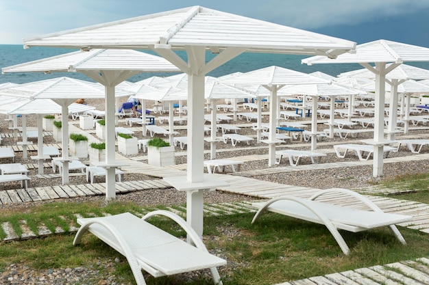 White wooden beach umbrellas paths and deck chairs on the seashore ocean