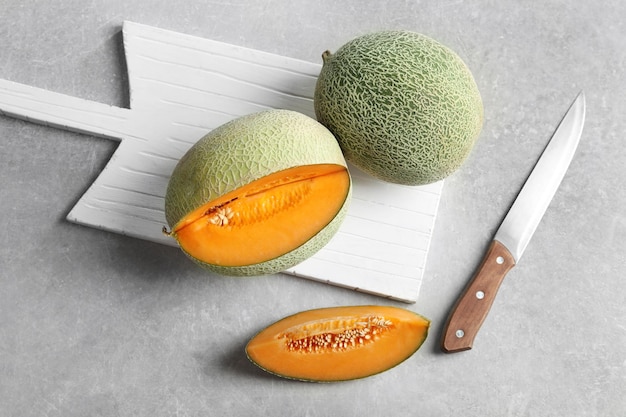 White wooden board with fresh ripe melons on grey table