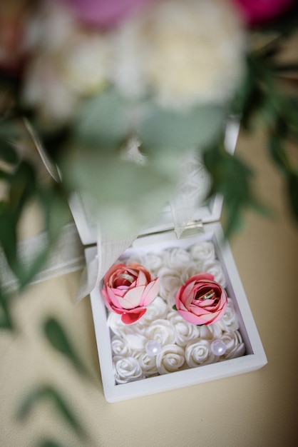 Photo white wooden box with two roses with wedding rings