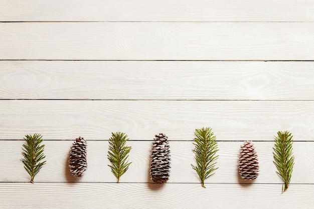 White wooden christmas background with fir branches and cones, top view, copyspace.