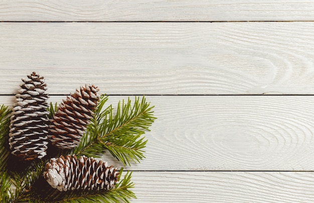 White wooden christmas background with fir branches and cones, top view, copyspace.