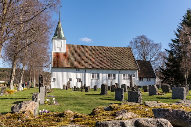 White wooden church in Sogne, a parish church in Sogne, Vest-Agder in Norway. Blue sky, green grass.