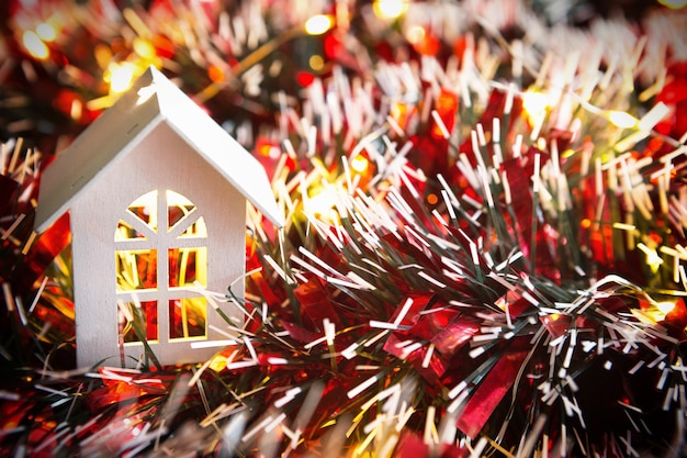 White wooden house with Christmas decorations, red tinsel and Golden lights garlands. New year, comfort, home warmth, cozy. Christmas background. Copy space