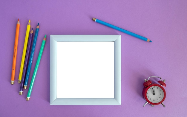 White wooden photo frame, colored pencils and a small alarm clock