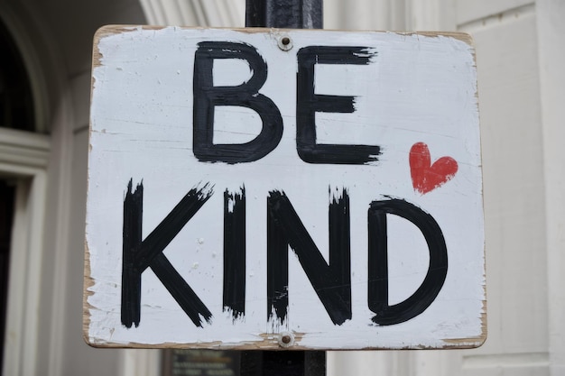 Photo a white wooden sign with black lettering reads be kind with a red heart