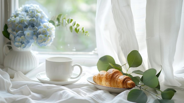 On a white wooden windowsill there is a bouquet of blue hydrangeas a cup of coffee and croissants