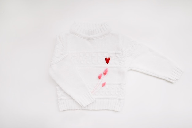 White woolen sweater with a red heart shaped pin on white background top view love romance fashion c