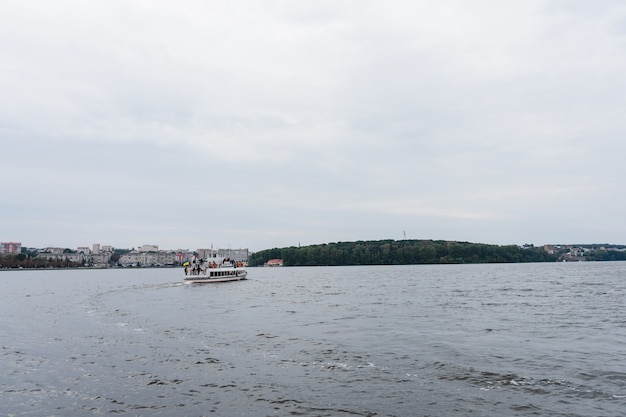 White yacht on the lake in summer day. Excursion yacht among the big lake on a background of green park.