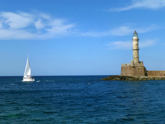 White Yacht Sailing near Historic Lighthouse at Old Venetian Harbor in Chania on Crete Island Greece