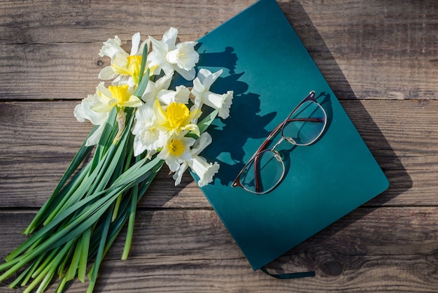 White and yellow daffodils, book and glasses on a wooden table