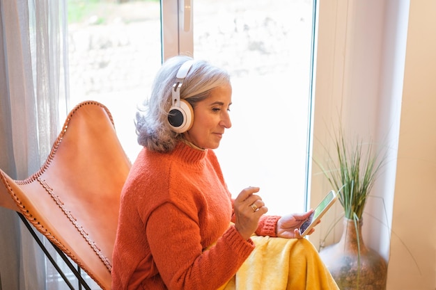 Whitehaired woman using music apps on her smartphone and listening to it on wireless headphones Concept Lifestyle music technology