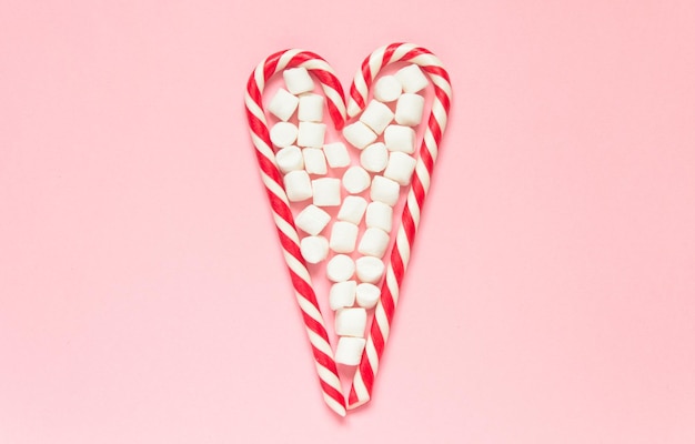 Whitered candy canes and marshmallow in heart shape on pink background