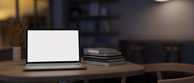 A whitescreen laptop computer mockup and books on a table in a modern dark room