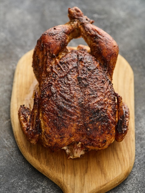 Whole barbecue chicken on a wooden board on a gray background