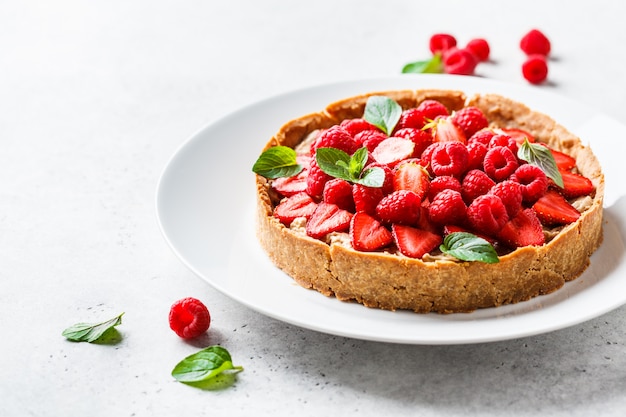 Photo whole berry tart with raspberries, strawberries and cream on white dish