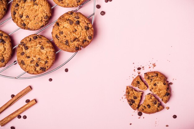 Whole and broken chocolate chip cookies and crumbs on pink background