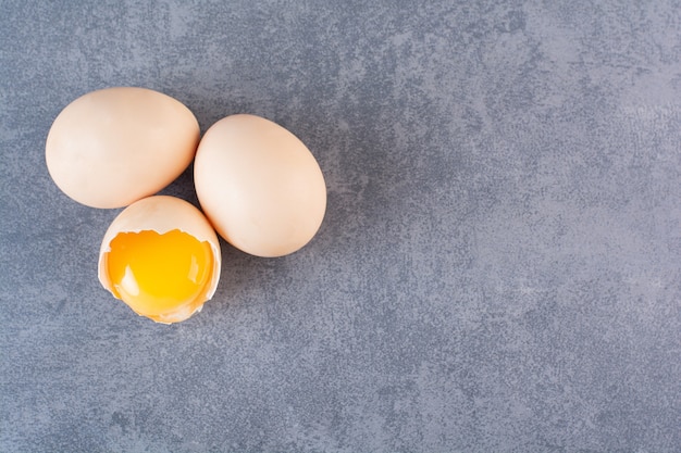 Whole and broken raw chicken eggs on stone table.