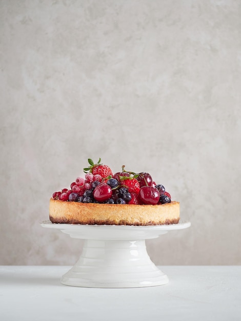 Whole cheesecake with fresh fruit on a white cake stand