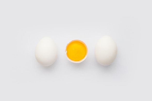 Whole chicken Eggs and cracked half with yolk on white background Minimalism