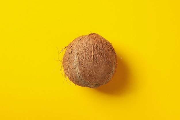 Whole coconut on yellow table, top view