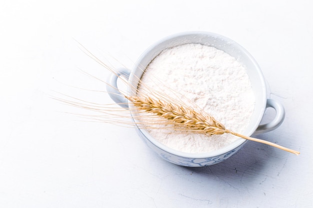 Whole flour in bowl with wheat ears on white background