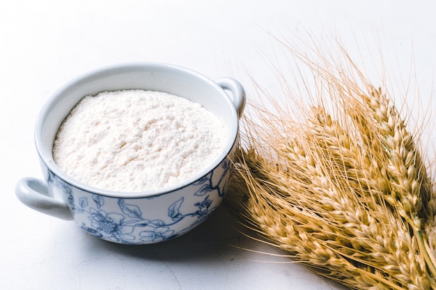 Whole flour in bowl with wheat ears on white 