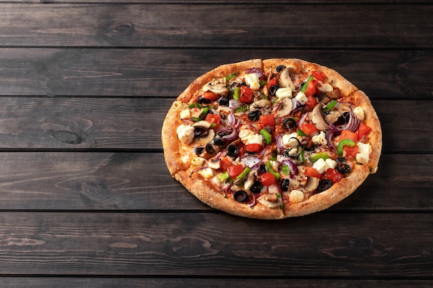 Whole fresh round pizza with chicken meat, vegetables, mushrooms and cheese close-up on a wooden brown table. tasty fast food surface in pizzeria with copy space