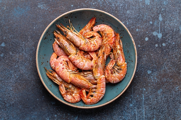 Whole fried big shrimps with seasonings in blue bowl on stone rustic background from above. Fresh cooked delicious grilled shrimps served on plate top view, healthy seafood meal