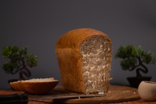 Whole grain bread lies on a kitchen wooden plate holding a golden cutting knife. Fresh bread.