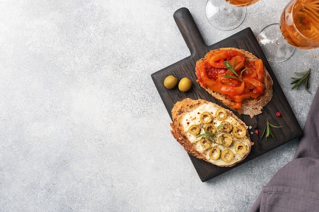 Whole grain bread sandwiches with cream cheese, olives and canned peppers with tomato on a wooden cutting Board.