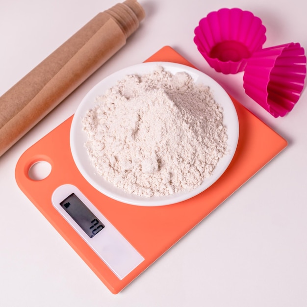 Whole grain flour sprinkled on a white plate on an orange kitchen scale on a white background