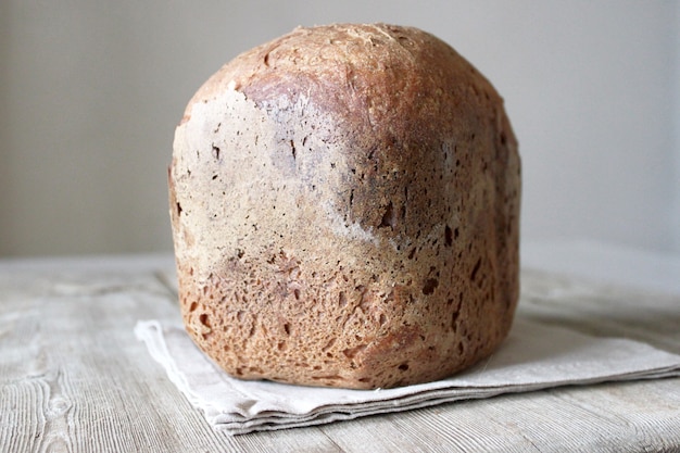 Photo whole grain rye wheat sourdough organic bread loaf on linen napkin on natural wooden table. homemade bread concept side view close up selective focus copy space