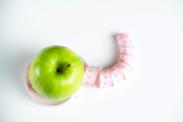 A whole green apple on a white background with a meter (measuring tape)