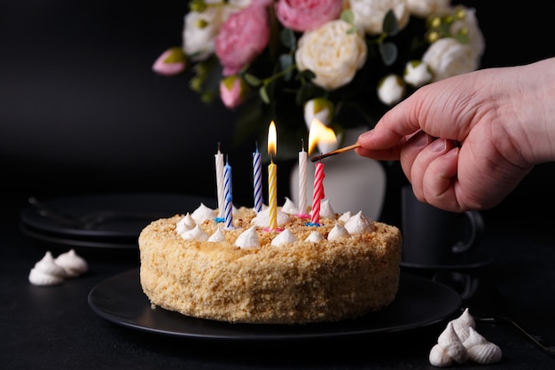 Whole holiday cake with crumbly shortcrust pastry and mini meringue Man lights candles on a cake Birthday cake with lit candles Homemade baking Black background selective focus closeup