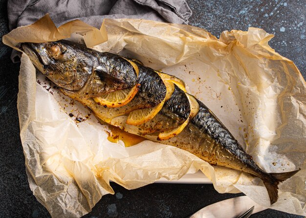 Whole mackerel or scomber fish with lemon and herbs baked and served on baking paper from above. Delicious roasted healthy fish on concrete background top view