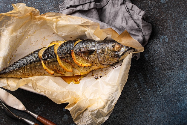 Whole mackerel or scomber fish with lemon and herbs baked and served on baking paper from above, free space for text. Delicious roasted healthy fish on concrete background top view