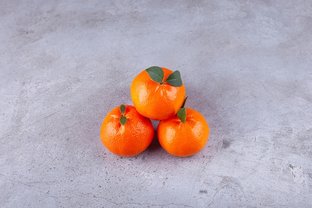 Whole orange fruits with green leaves placed on stone background. 