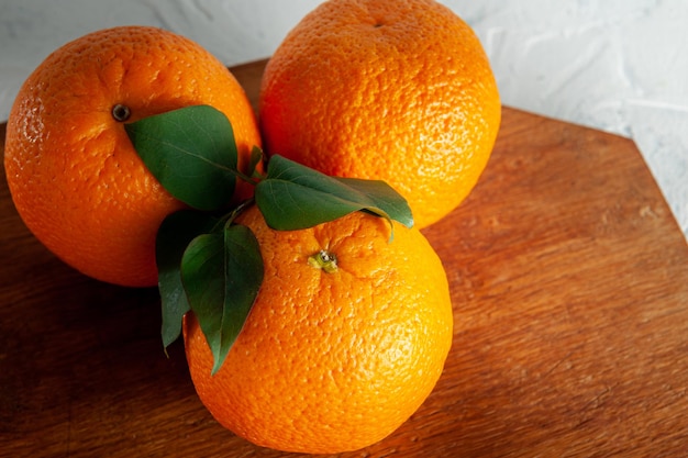 Whole oranges on a wooden board on a white background with green leaves top view