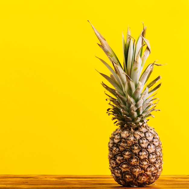 Whole pineapple on table against yellow background