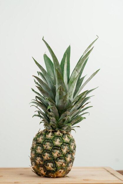 Photo a whole pineapple on a wooden surface against a light background