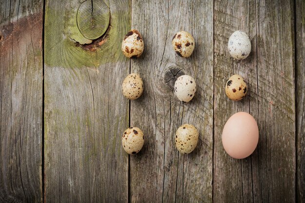 Whole quail and chicken eggs in a small castiron frying pan on the background of an old wooden texture