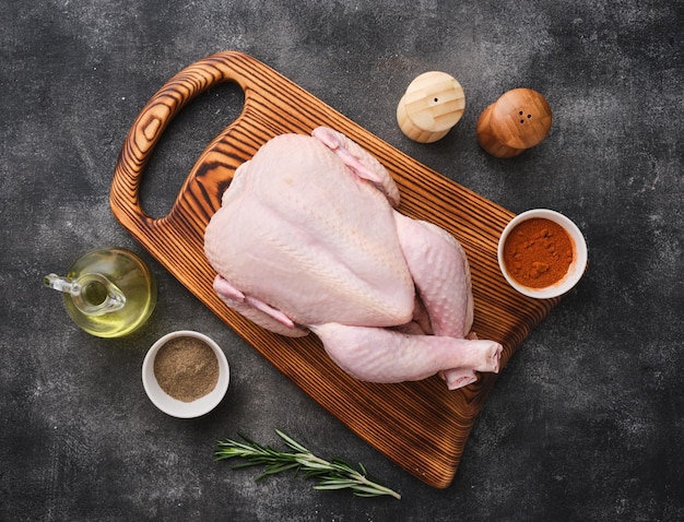 Whole raw chicken on wooden board on dark background Preparing raw chicken Top view