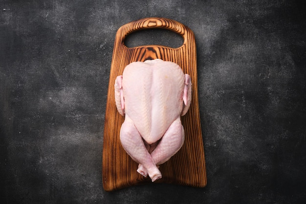 Whole raw chicken on wooden board on dark background Preparing raw chicken Top view