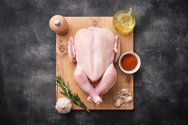 Whole raw chicken on wooden board on dark background Preparing raw chicken Top view