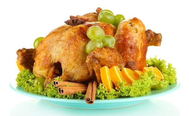 Whole roasted chicken with lettuce grapes oranges and spices on blue plate isolated on white