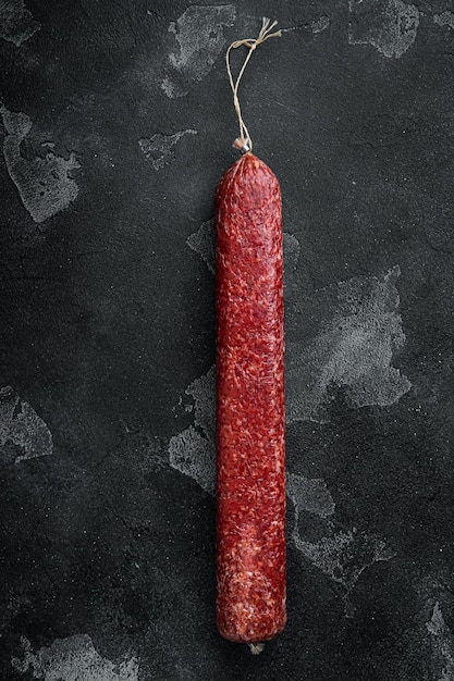 Whole sausage salami on black dark stone background top view flat lay with copy space for text